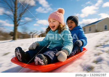 Children Enjoying Winter Fun While Sledding Down a Snowy Hill Under a Clear Sky Children Enjoying Winter Fun While Sledding Down a Snowy Hill Under a Clear Sky 132002397