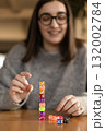 Female hands stacking colorful dice into a pyramid while a smiling woman appears in the background. Teamwork and concentration concept. 132002784