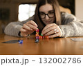 Young woman leaning over the table while stacking colorful dice into a pyramid. Concentration and creativity concept. 132002786
