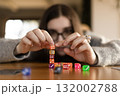 Young woman carefully stacking colorful dice one on top of another. Concentration and precision concept. 132002788