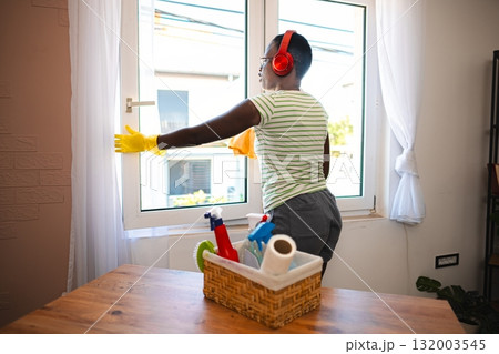 Woman cleaning windows while listening to music with headphones at home Woman cleaning windows while listening to music with headphones at home 132003545