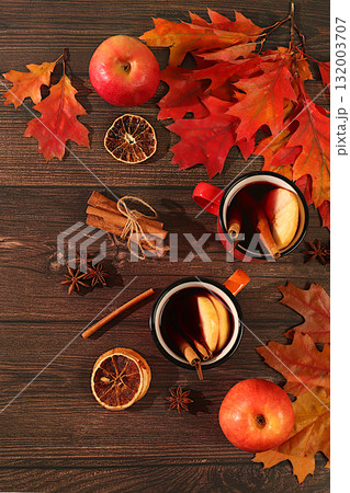 Two colorful enamel mugs with hot autumn drink, mulled wine with apples and autumn fallen leaves, star anise, cinnamon on a wooden table, banner for display, autumn greeting concept, mockup for menu 132003707