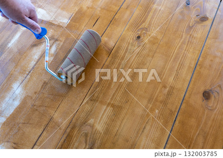 Hand applying varnish on wooden floor with roller for smooth finish 132003785