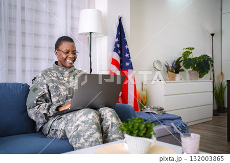 American female soldier working on laptop at home with United States flag in background 132003865