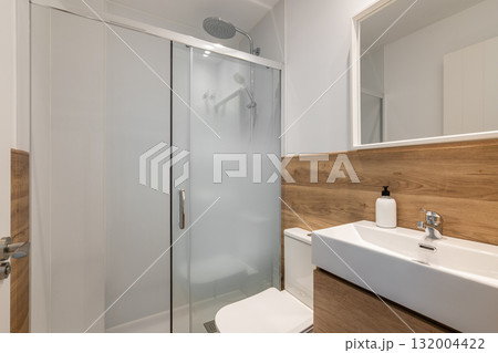 Modern bathroom with a glass shower, wooden accents, and a sleek sink. Bright and clean design with minimalistic decor. 132004422