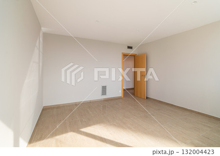 Empty room with light-colored walls and wooden floor. A single door leads to another space. Natural light enters through a window, creating a bright atmosphere. 132004423