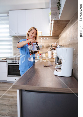 Smiling nurse pouring coffee in kitchen during work break 132005266