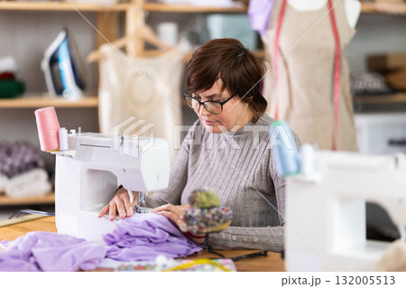 Working in sewing workshop - female dressmaker working at sewing machine making stitches on fabric 132005513