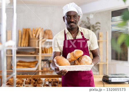Portrait of male baker with bread and baguettes in hands in bakery 132005573