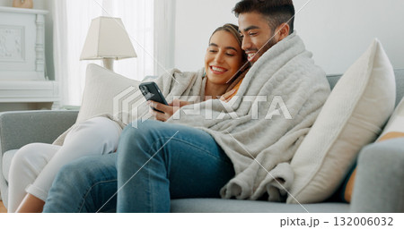 Happy couple, relax and post on social media with phone or communication, app or reading news together in home. Movie, video or streaming online with man and woman in living room with blanket on sofa Happy couple, relax and post on social media with phone or communication, app or reading news together in home. Movie, video or streaming online with man and woman in living room with blanket on sofa 132006032