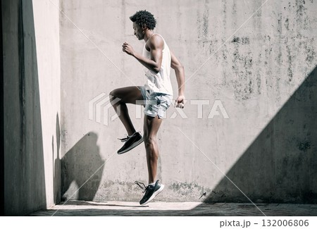 Exercise, fitness and black man jump in city for health, wellness and energy against wall mockup. Sports, training and male athlete jumping, workout or exercising for endurance, practice or strength. Exercise, fitness and black man jump in city for health, wellness and energy against wall mockup. Sports, training and male athlete jumping, workout or exercising for endurance, practice or strength. 132006806