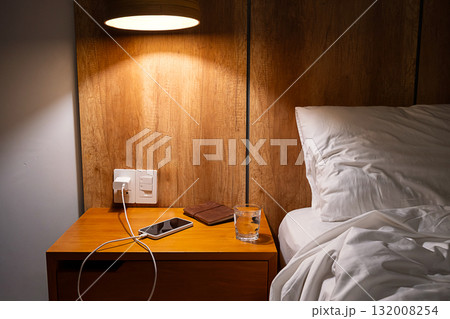 Mobile phone charging on bedside table in comfortable hotel or home bedroom. Mobile phone charging on bedside table in comfortable hotel or home bedroom. 132008254