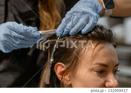 A stylist applies hair dye with precision while a client relaxes in the salon chair. The atmosphere is calm and professional. 132009417