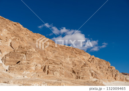 Golden rock formations rise majestically against a backdrop of fluffy white clouds and a bright blue sky in the Sinai desert Golden rock formations rise majestically against a backdrop of fluffy white clouds and a bright blue sky in the Sinai desert 132009465