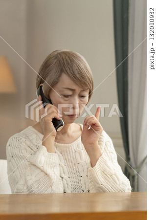 家の電話にかかってきた不信な電話に対応するシニア女性 132010932