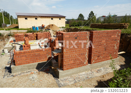 Brick walls are rising at a construction site, supported by wooden forms and metal rods. Brick walls are rising at a construction site, supported by wooden forms and metal rods. 132011223