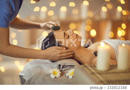 Relaxed young woman is getting beauty face massage with facial roller at spa salon Relaxed young woman is getting beauty face massage with facial roller at spa salon 132012188