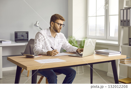 Businessman using laptop and making notes on paper in his office 132012208