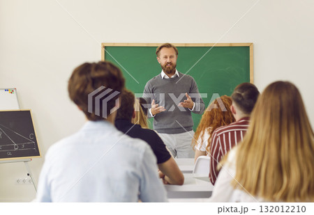 Math teacher standing in classroom and talking to group of school or college students Math teacher standing in classroom and talking to group of school or college students 132012210