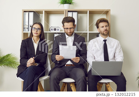 Group of young business people sitting on chairs in a row with resumes and laptop. 132012215