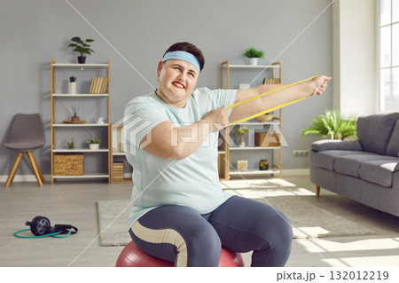 Happy overweight woman training with resistance band at home 132012219