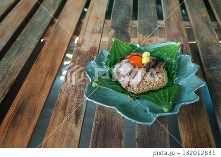 Steamed sticky rice wrapped in lotus leaf, filled with minced pork, ginkgo, Chinese sausage, and salted egg yolk on an antique wooden table 132012831