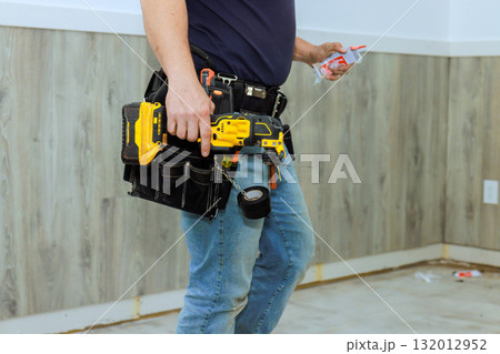 Worker holds power drill supplies while preparing for renovation in bare room with wooden walls. 132012952