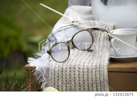 Cozy scene featuring glasses, a knitted scarf, and a cup of tea, perfect for relaxation. Cozy scene featuring glasses, a knitted scarf, and a cup of tea, perfect for relaxation. 132013075