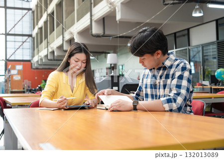 Young Asian students using laptop, learning and discussing in a library at the university. 132013089