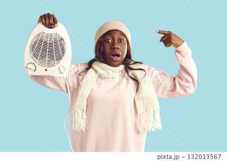 Shocked worried woman pointing finger to electric heater and looking at camera on blue background. Shocked worried woman pointing finger to electric heater and looking at camera on blue background. 132013567