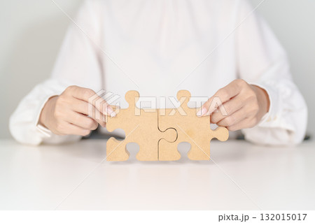 Woman connecting couple puzzle piece, wood jigsaw on table. Business solutions, mission, success, goals, strategy, Teamwork, Idea, Solution and challenge concepts Woman connecting couple puzzle piece, wood jigsaw on table. Business solutions, mission, success, goals, strategy, Teamwork, Idea, Solution and challenge concepts 132015017