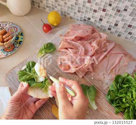 Anonymous person makes sandwich with sausage, lettuce, and mortadella, homemade mayonnaise in kitchen. Italian cuisine, high-quality farm-grown ingredients. 132015527