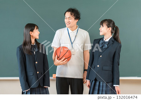 教室の黒板の前にいるバスケットボールを持つ男性教師とブレザー姿の女子生徒 132016474