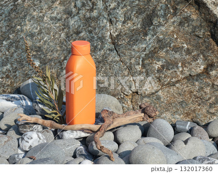 Plastic orange beauty bottle against backdrop of natural elements. Cosmetics and facial and hair care. Mock-up template for design. Eco-friendly products. Background, design composition. 132017360