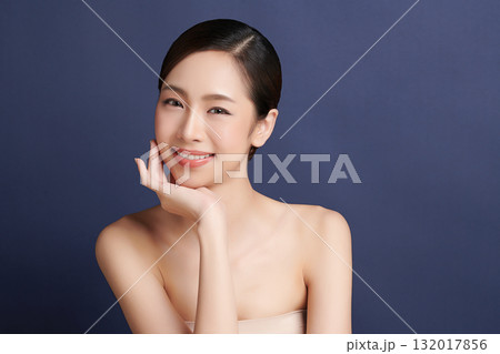A beautiful young Asian woman with clean, fresh skin against a blue background. Skincare, facial treatment, cosmetology, beauty, and spa. An elegant portrait of an Asian woman. 132017856
