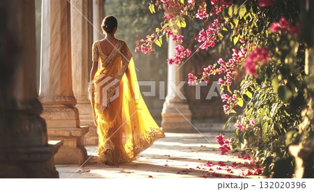 Indian woman in a yellow sari walking through an ancient garden, dappled sunlight illuminating her path, pink bougainvillea flowers creating a vibrant, cultural scene 132020396