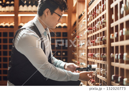 Professional Sommelier Selecting Fine Wine Bottle in Traditional Wooden Cellar 132020773