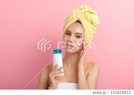Young woman applies lotion on cheek showing blank tube 132020812