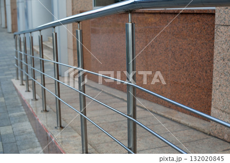 Modern stainless steel railing with smooth, polished lines, set against a textured granite wall. Architectural feature is part of contemporary building design, showcasing minimalist style 132020845