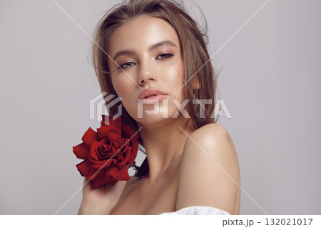 Pretty woman holds red rose flower by chin looking at camera Pretty woman holds red rose flower by chin looking at camera 132021017