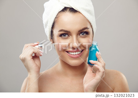 smiling woman applies facial serum standing on a grey isolated background, close up beauty portrait. smiling woman applies facial serum standing on a grey isolated background, close up beauty portrait. 132021023