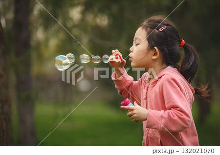 Young Girl Blowing Soap Bubbles in Park Young Girl Blowing Soap Bubbles in Park 132021070