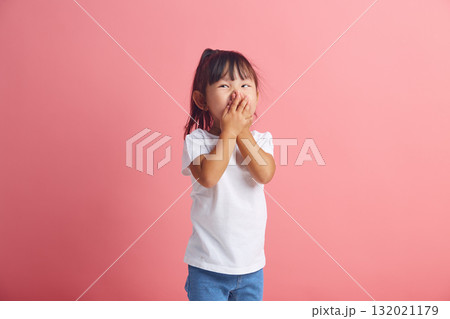 Little vivacious beautiful asian girl giggles joyfully, covers mouth, has a fun standing against pink background.  132021179