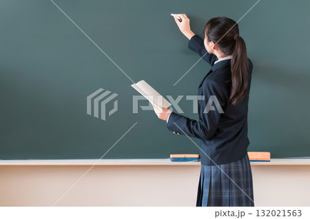 教室の黒板にチョークで文字を書く中学生の女子生徒 132021563