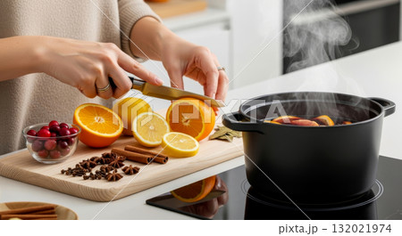Woman cutting an orange for steaming mulled wine with cloves, cinnamon, and star anise. Cozy winter drink preparation. 132021974