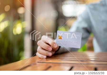 Close up of a hand holding or showing a credit card while sitting at wooden table in cafe. Bank ads. Close up of a hand holding or showing a credit card while sitting at wooden table in cafe. Bank ads. 132022230