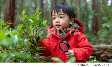 A young boy explores nature with a magnifying glass, examining a lush green plant while fostering a love for learning in the forest 132022453