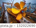 Massive yellow propeller at shipyard. Ship construction and marine engineering visible in dry dock with cranes in the background 132022690