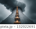 A cooling tower rises into a moody sky, its industrial architecture contrasting with the vapor and light accentuating the tower's height 132022691