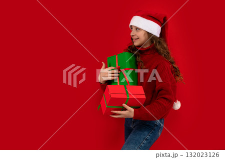 Girl in Santa hat holds presents and looks aside Girl in Santa hat holds presents and looks aside 132023126